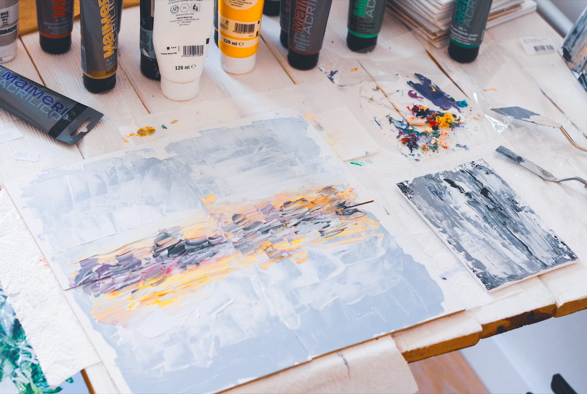 Abstract painting in white, yellow, and purple sitting on a table drying.