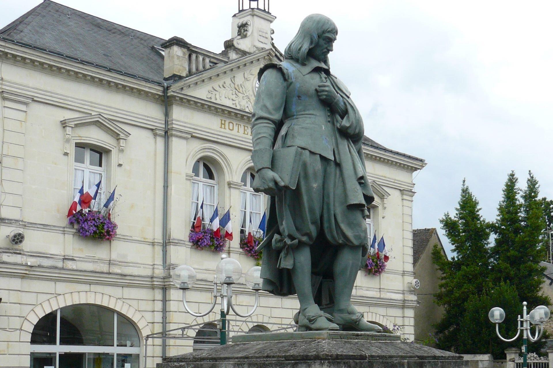 Statue of René Descartes standing in front of a town hall building with French flags and flowers