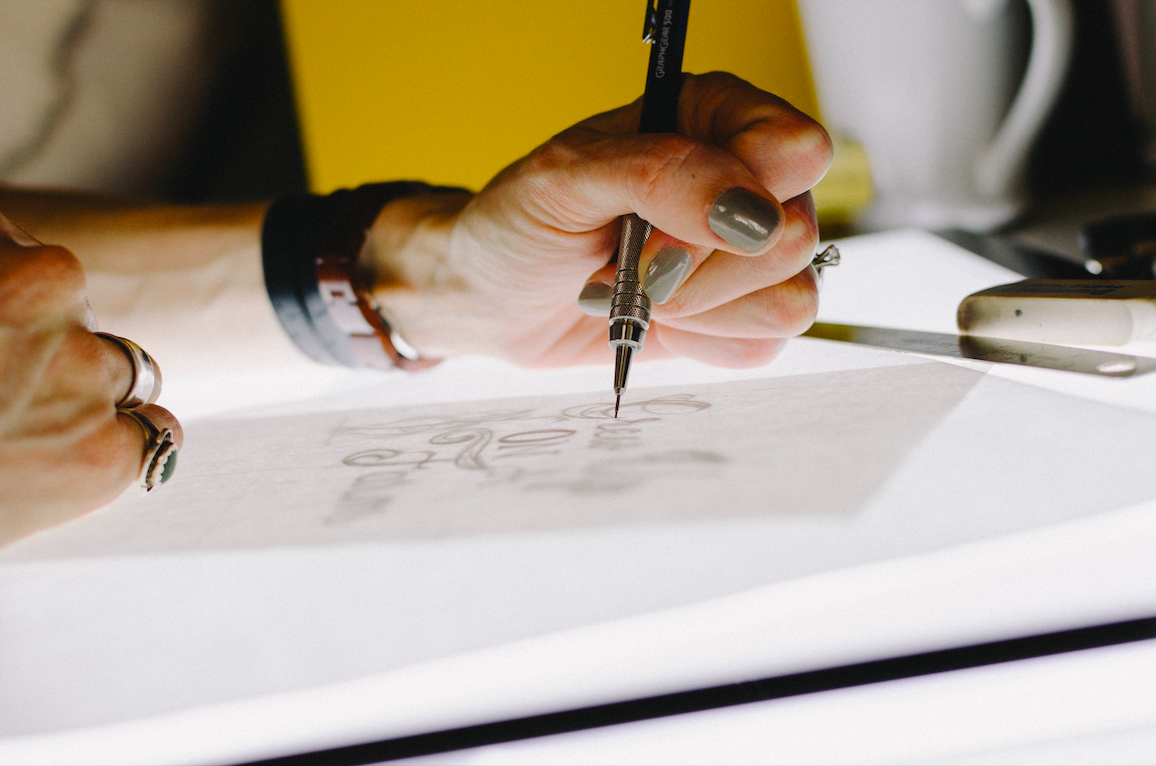 A hand hovering over a drawing on a tracing table.