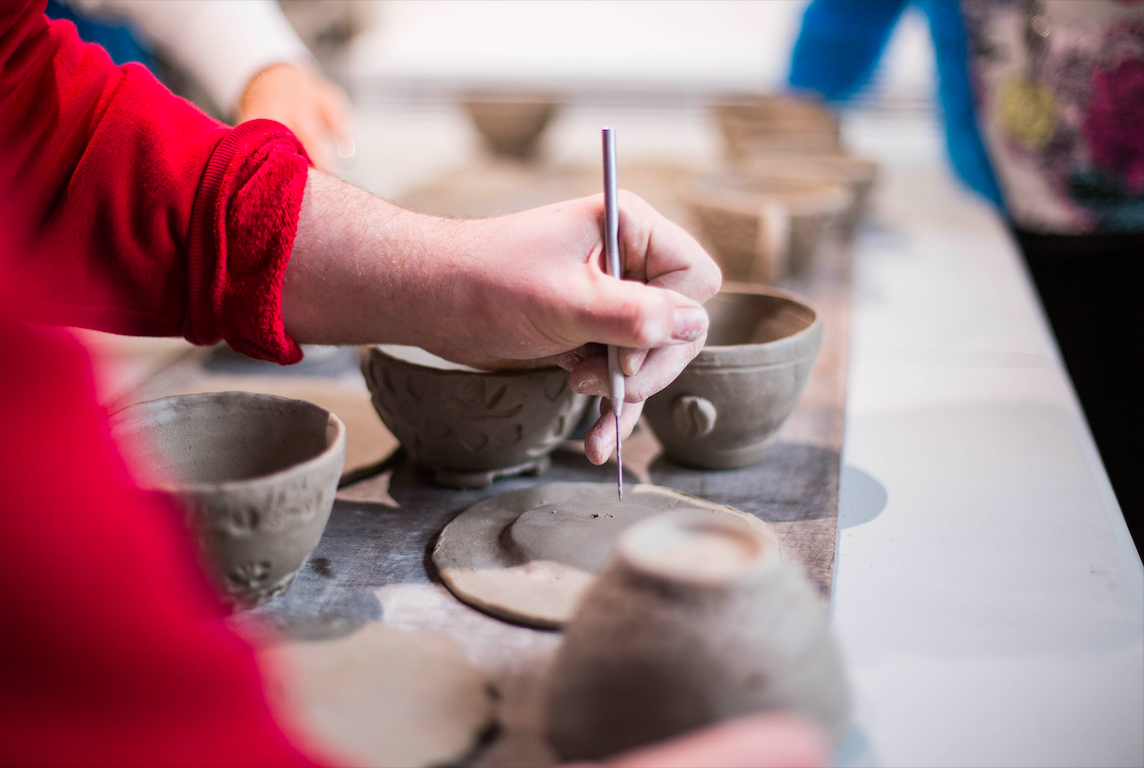 Person carving details on clay works.