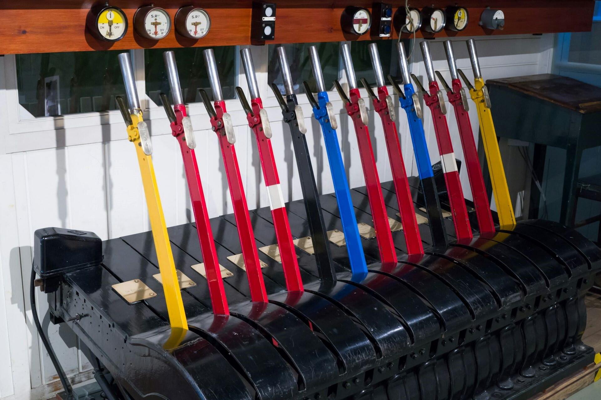 Row of colorful mechanical lever controls connected to a large machine mechanism