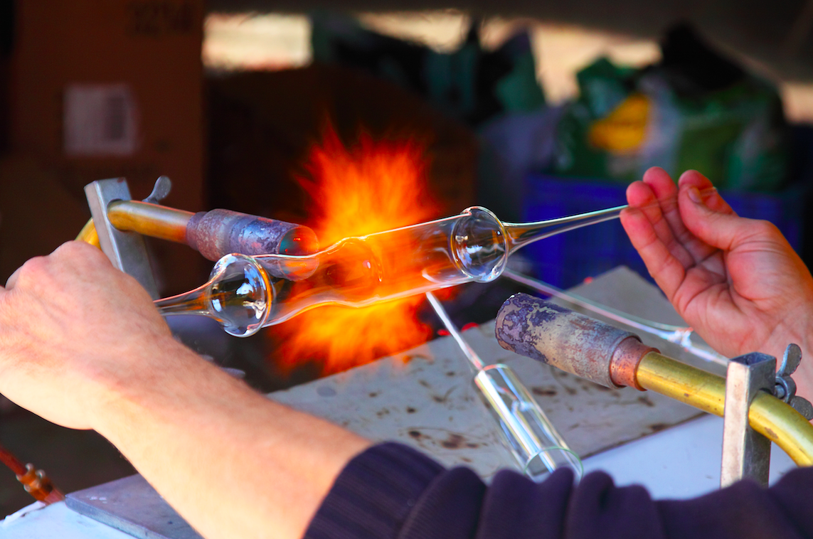 Person holding thin glass tube in front of a fire.
