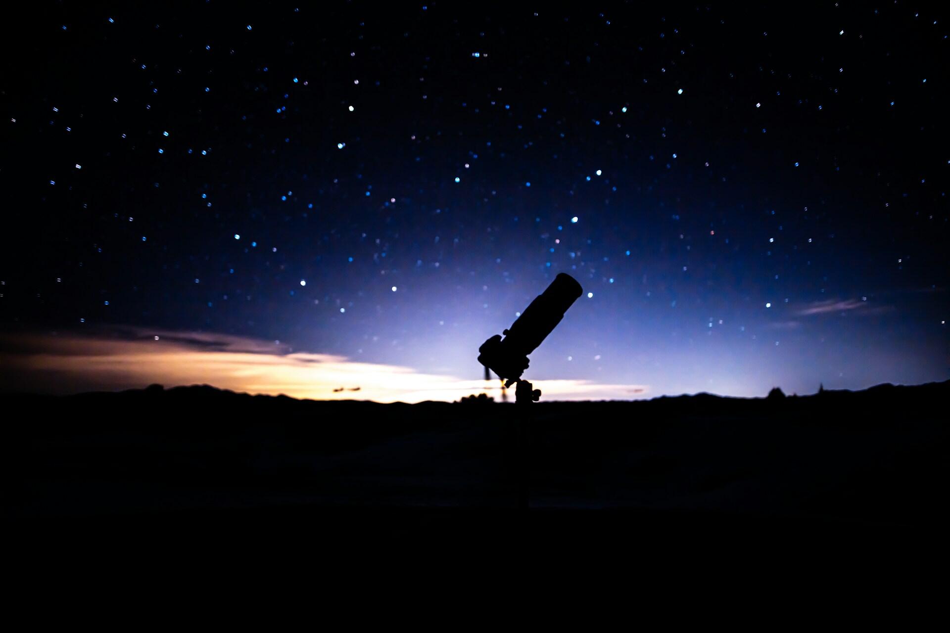 Telescope pointed at a starry night sky above a landscape