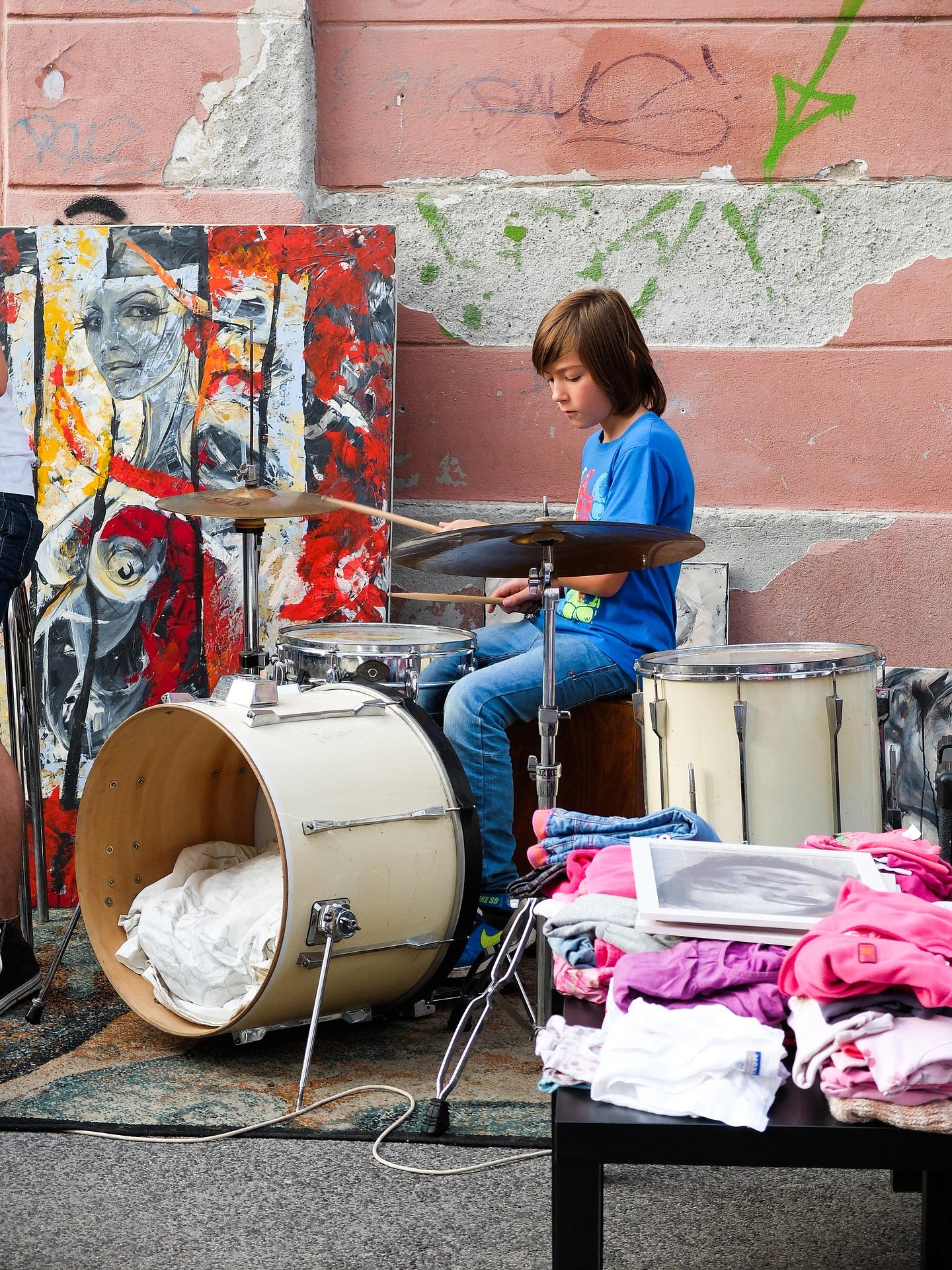 Kid playing a drum set outside in front of a wall