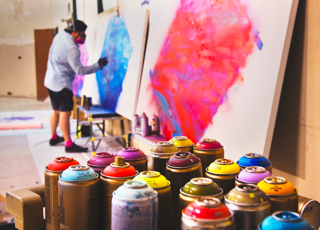 Man spray-painting on a large canvas.