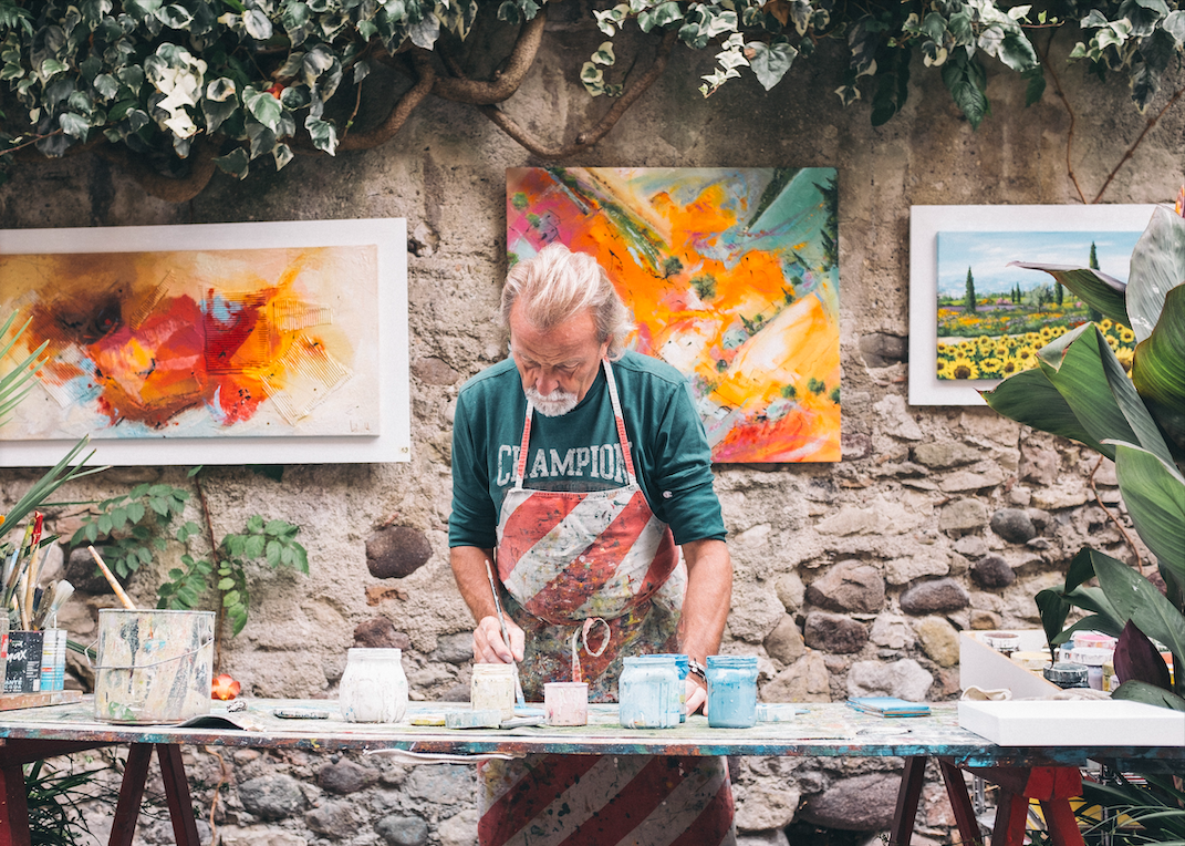 Old man standing next to a table painting.