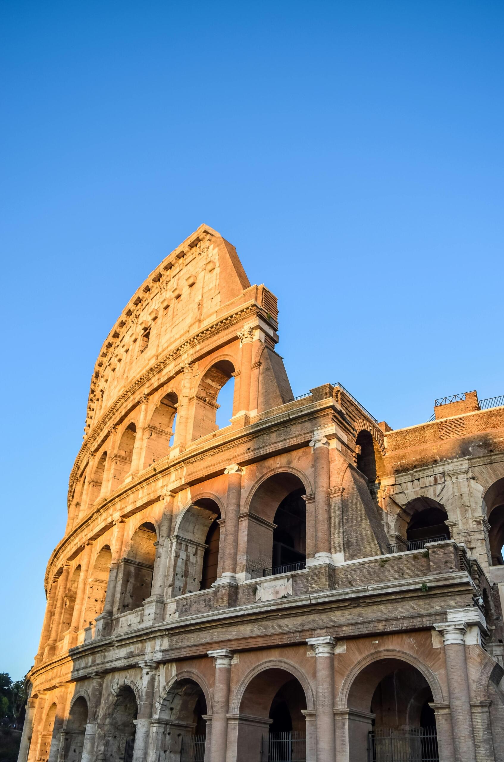 The Colosseum in Rome under a clear blue sky, showcasing its ancient arches and iconic structure.