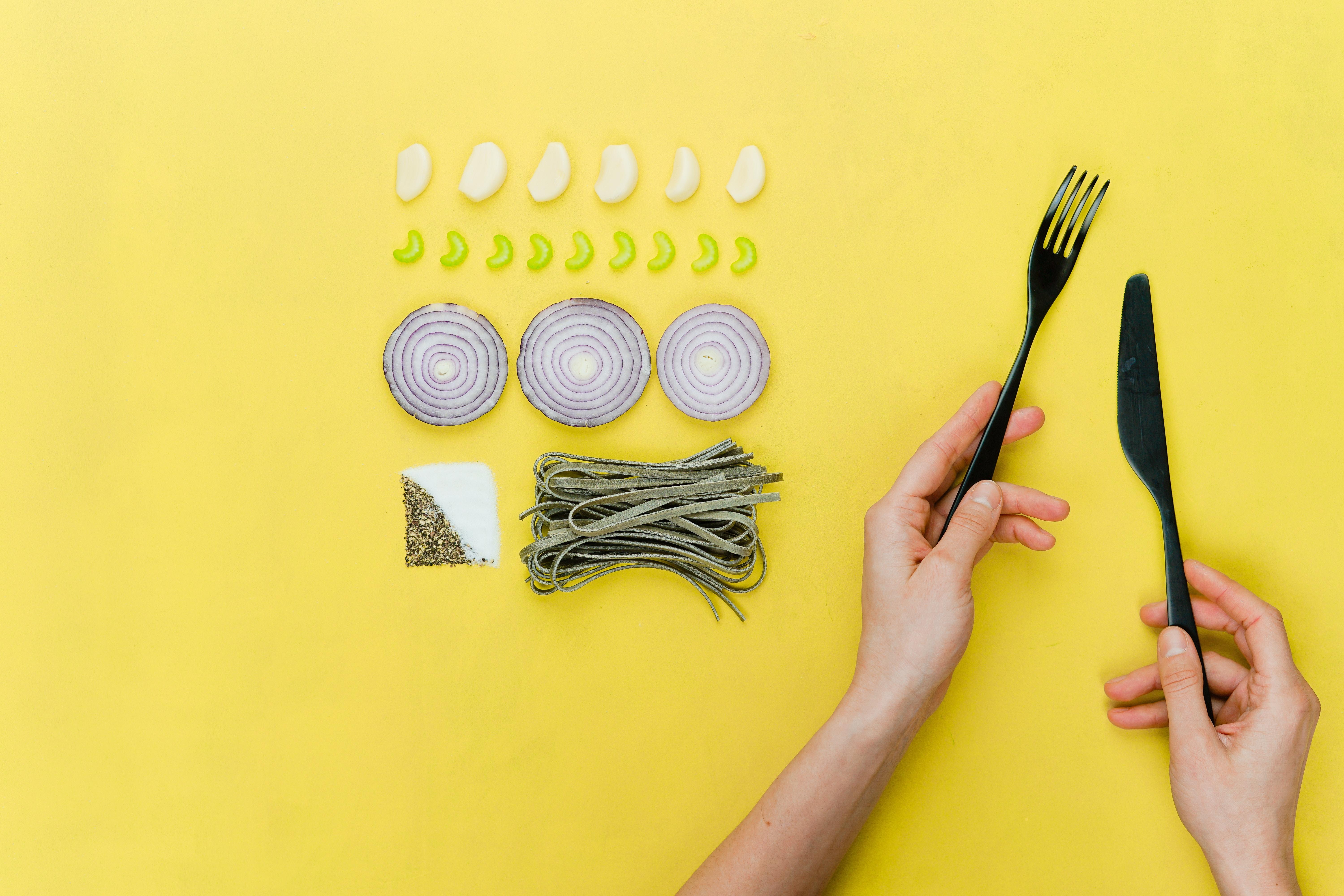 Vegetables and hands holding a knife and fork on a yellow background