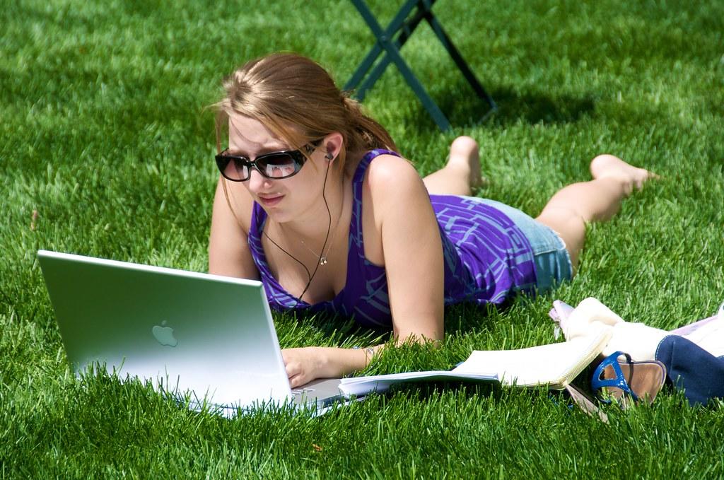 A student studies with her laptop and books in the park.