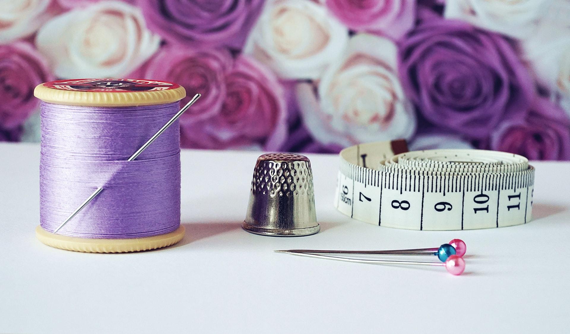 Purple thread, a thimble, and measuring tape on a white table.