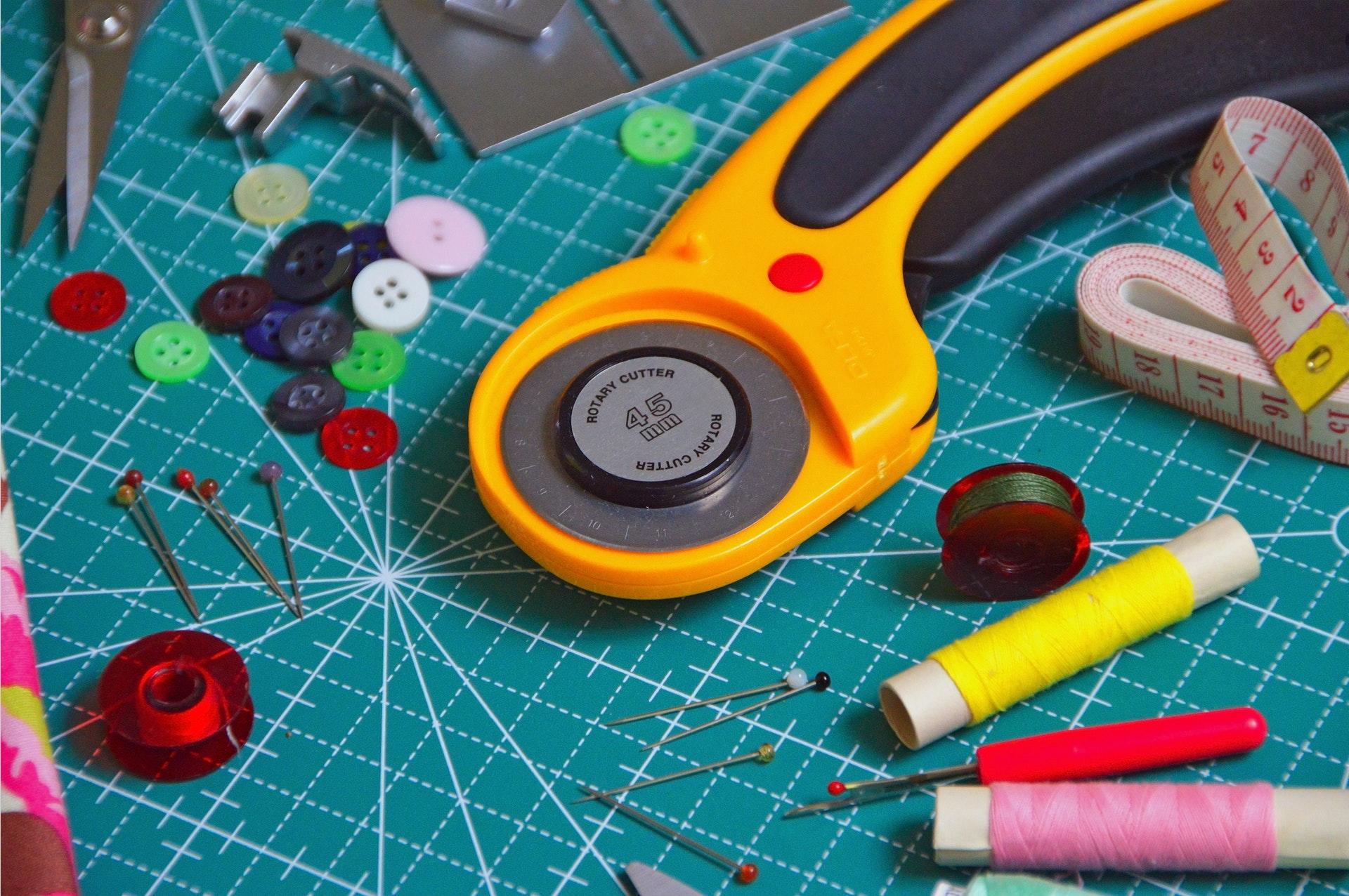 Sewing pins, buttons, thread, and bobbins on a measuring board.