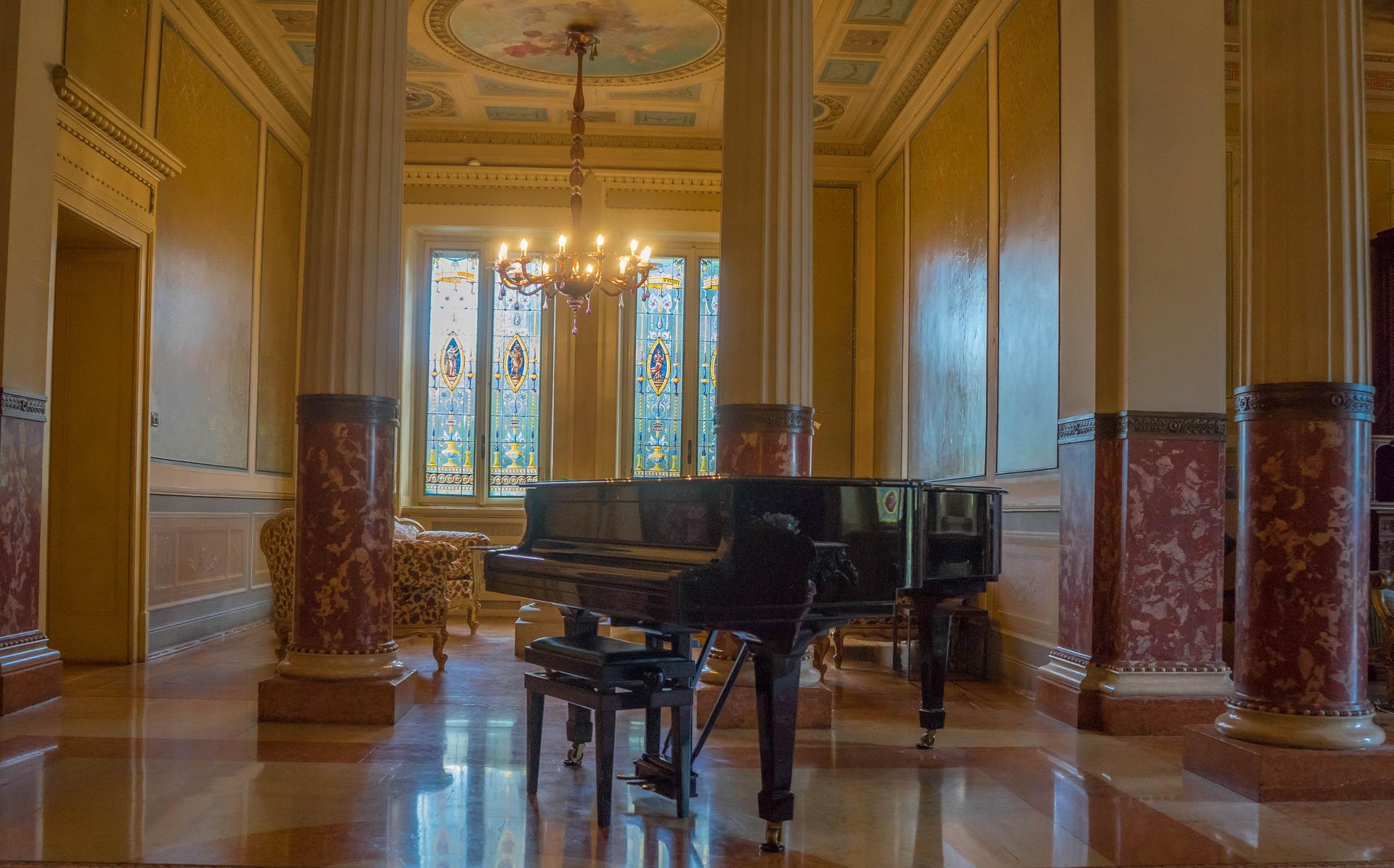A Victorian décor piano in the middle of floral patterned pillars. There is a chandelier hanging in the middle of the room. In addition to self-discipline, the benefits of piano also include enhancing the aesthetic sense of your house
