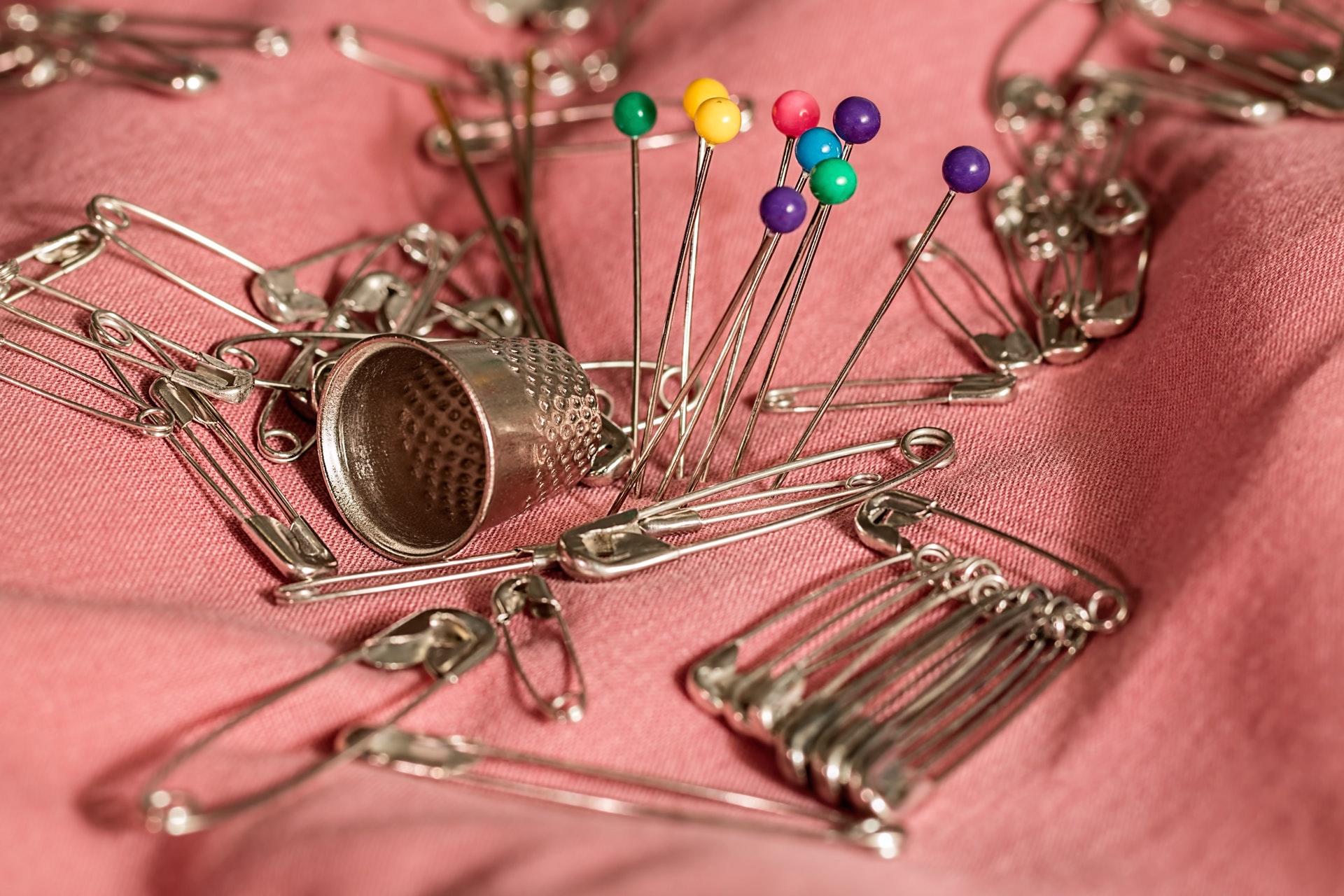 Safety pins, thimble, and sewing pins sitting on pink fabric.