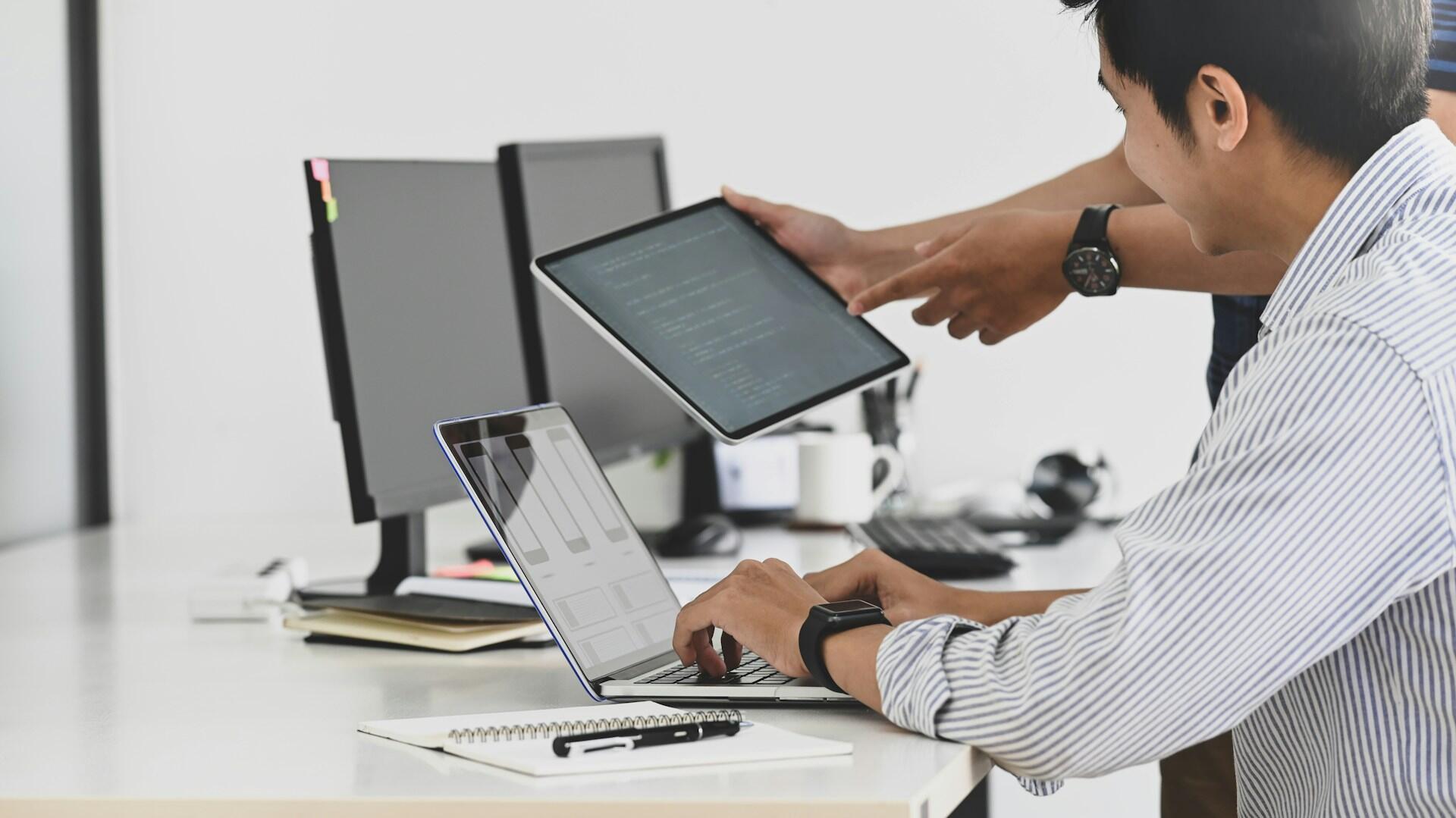 Two guys looking at IT software on a computer and iPad.