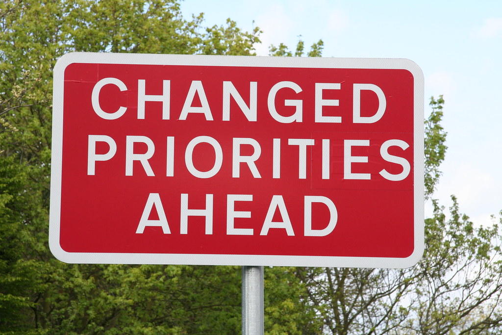 A sign reads 'Changed Priorities Ahead'.
