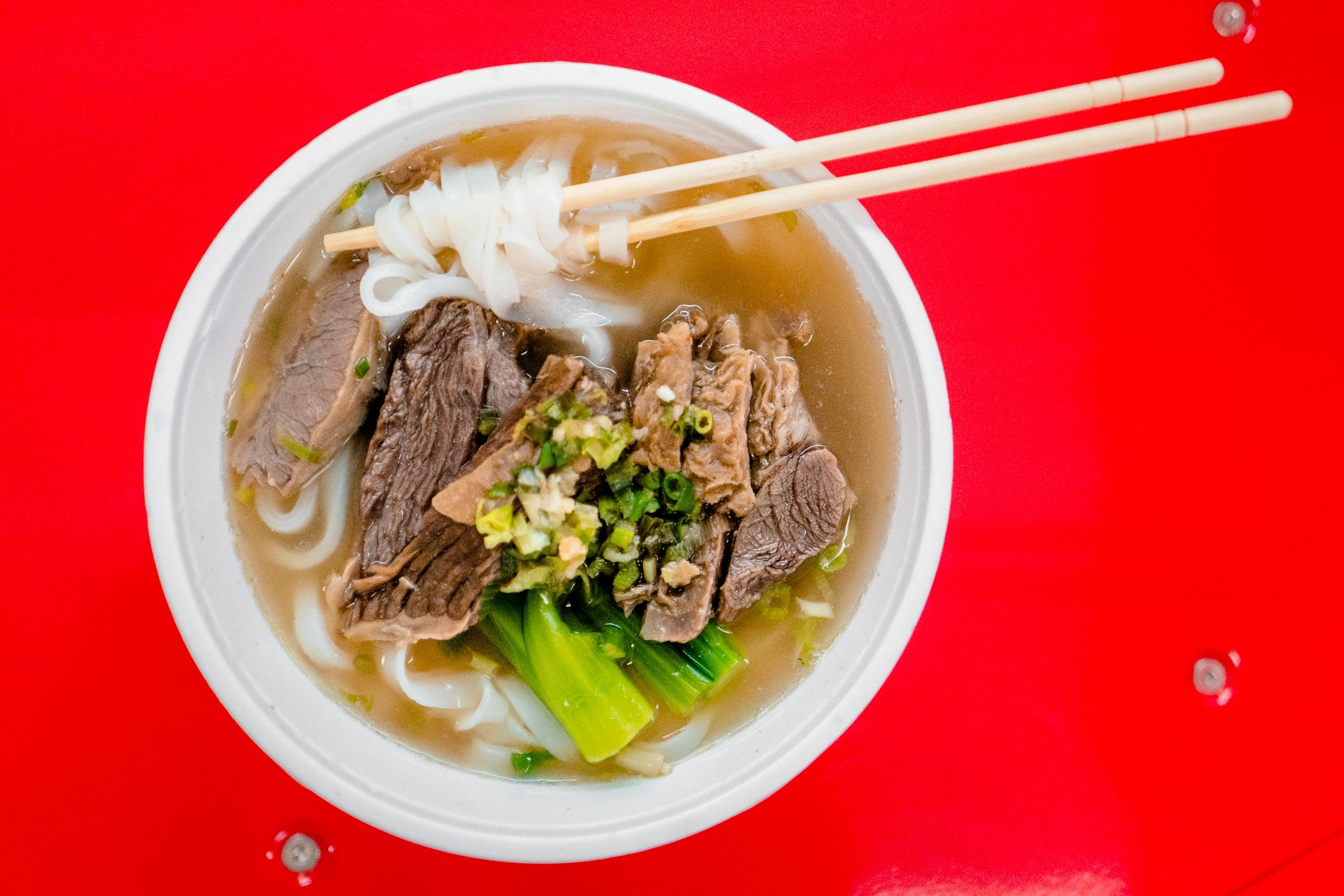 A bowl of ramen noodles sitting over a red tabletop.