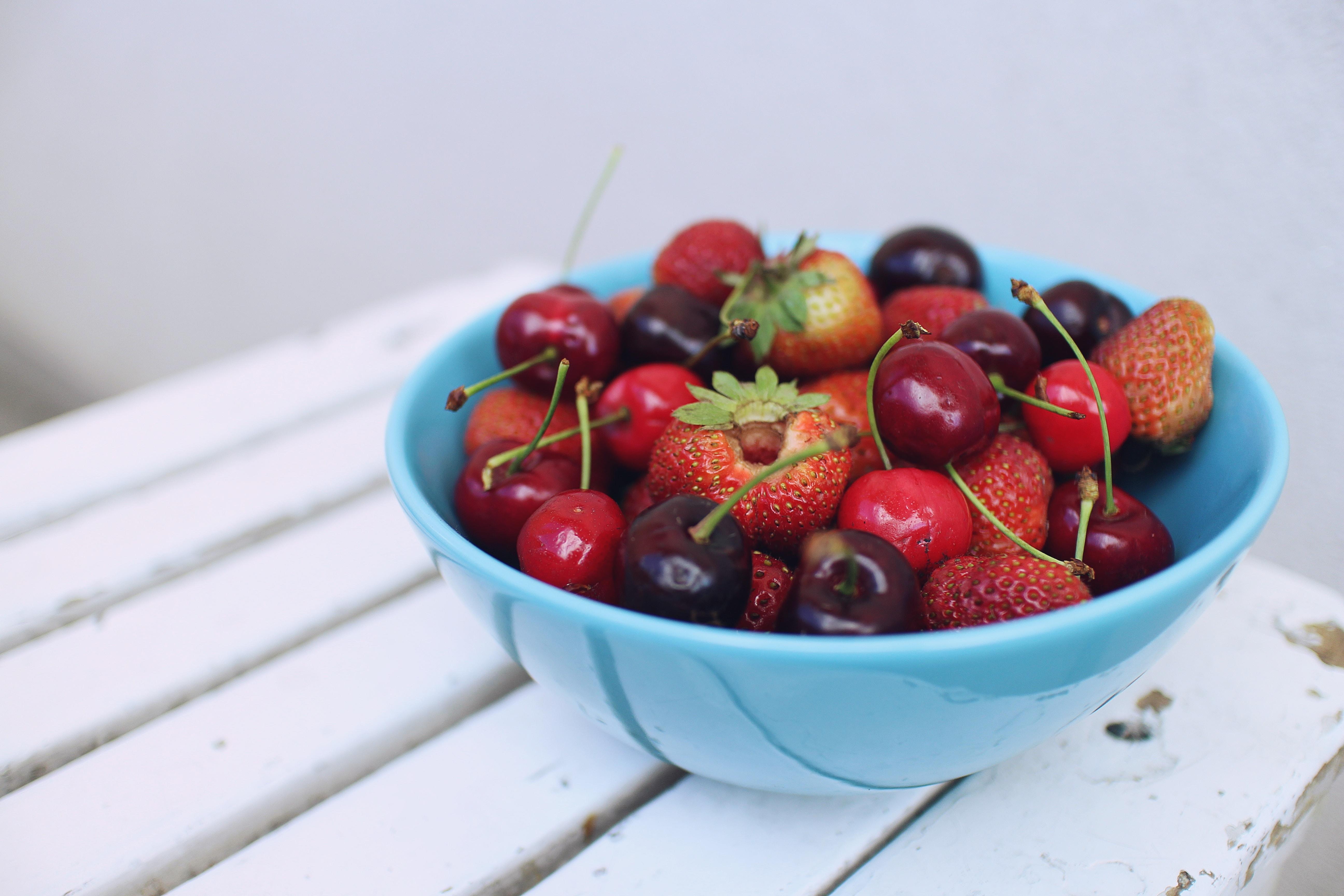 A bowl of red strawberries and cherries, sitting in a blue bowl. 