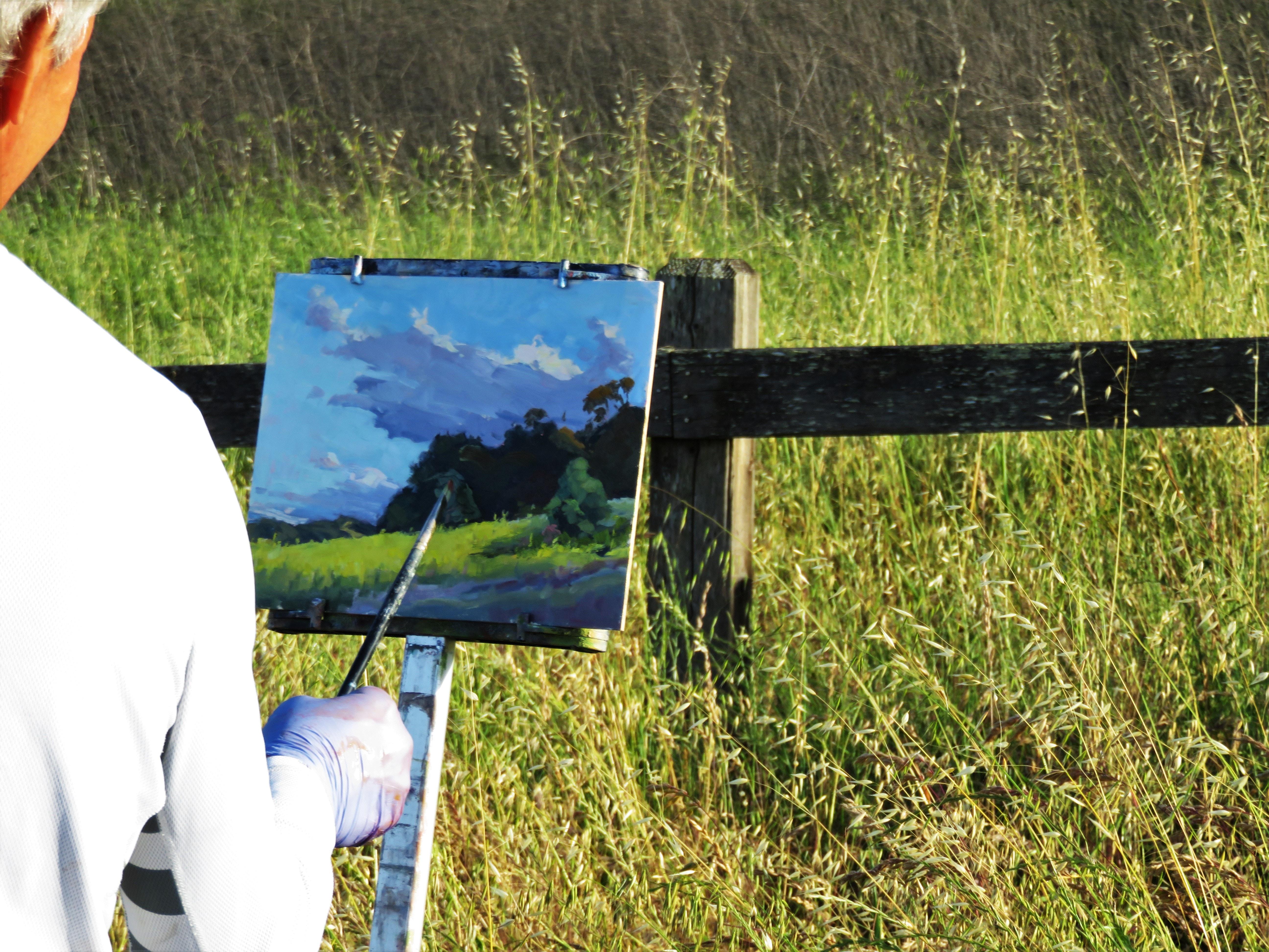 Man painting in front of a green grass field.