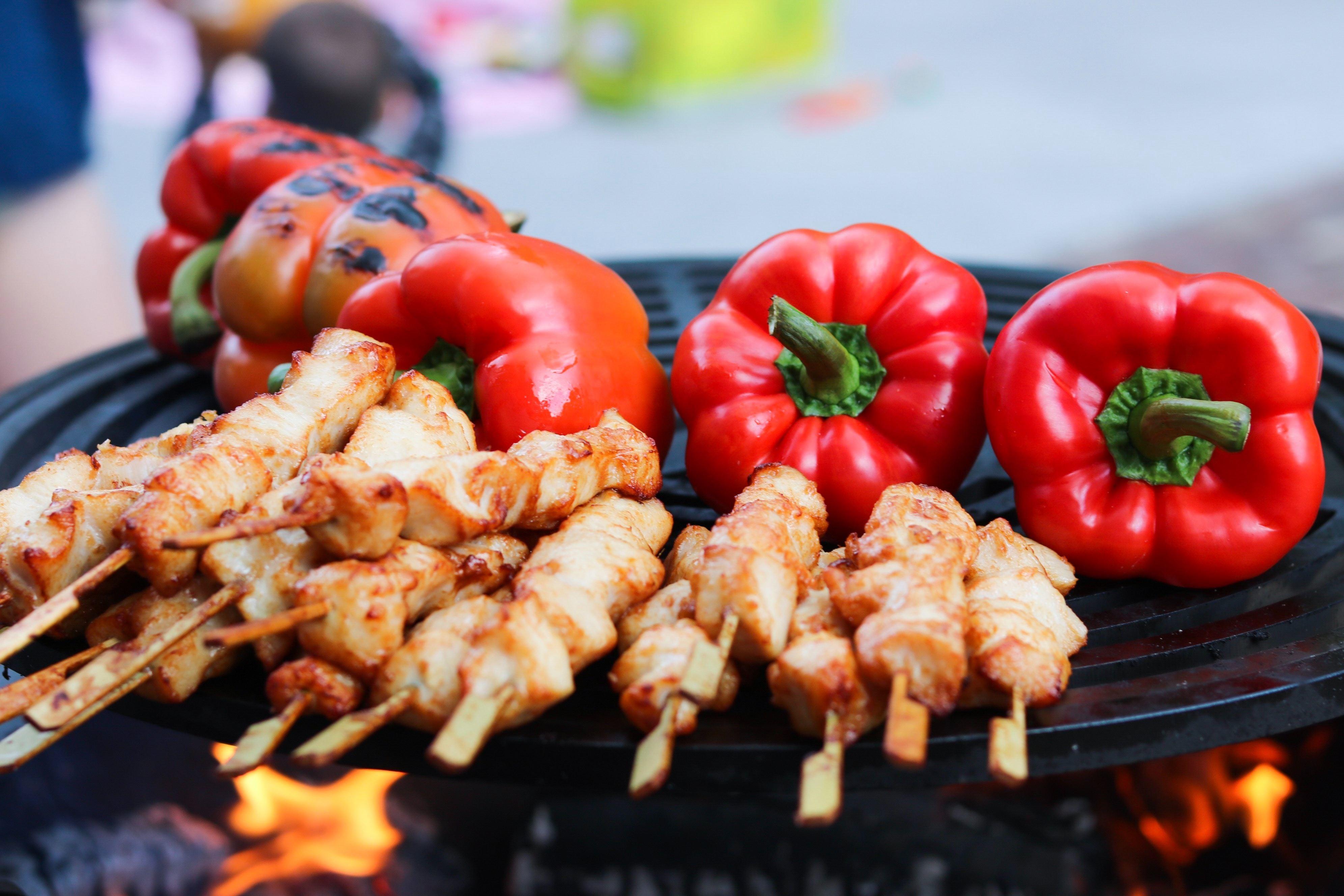 Red bell peppers and pork being cooked on a grill