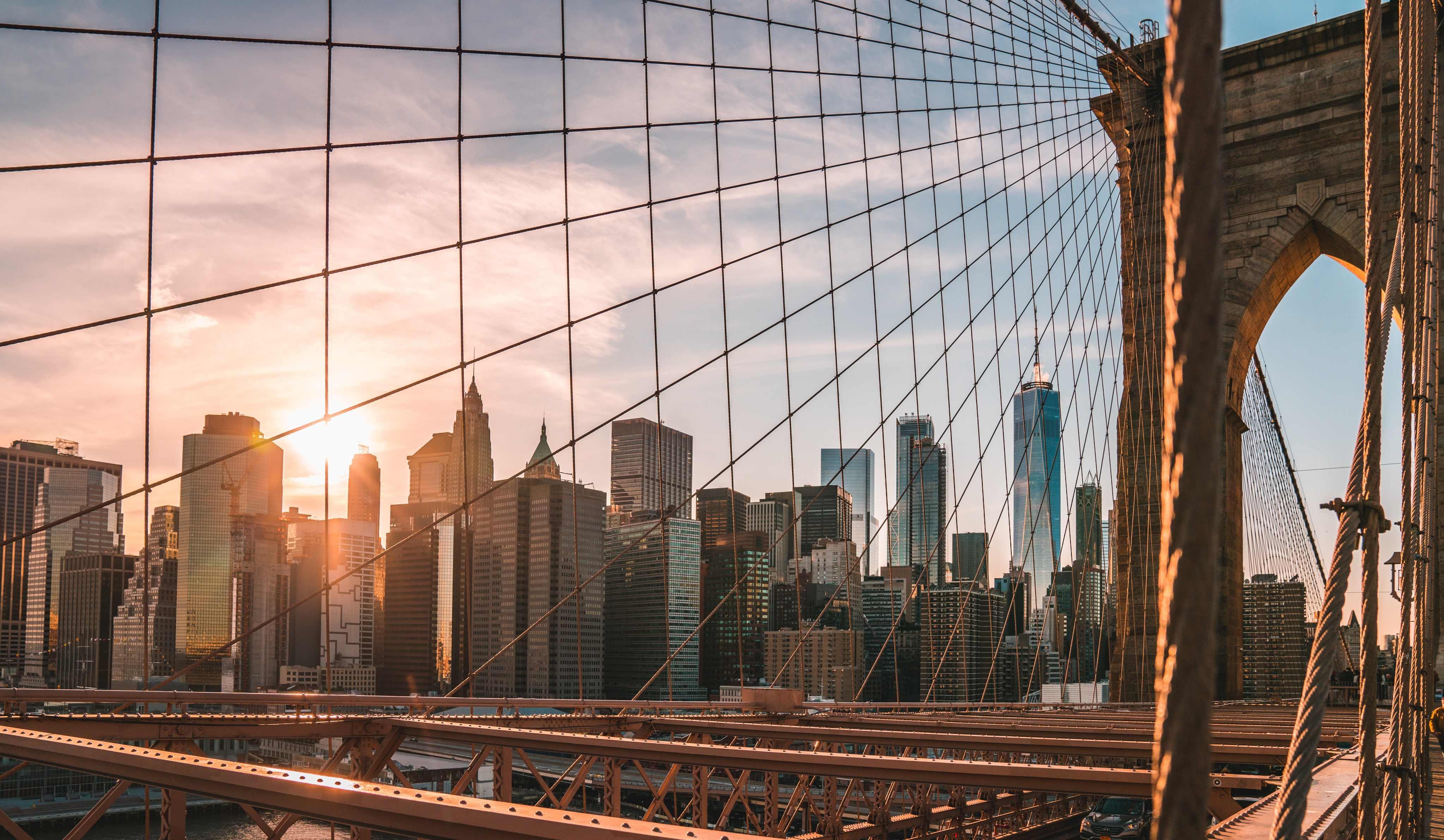View of the NYC skyline through the Brooklyn Bridge at sunset