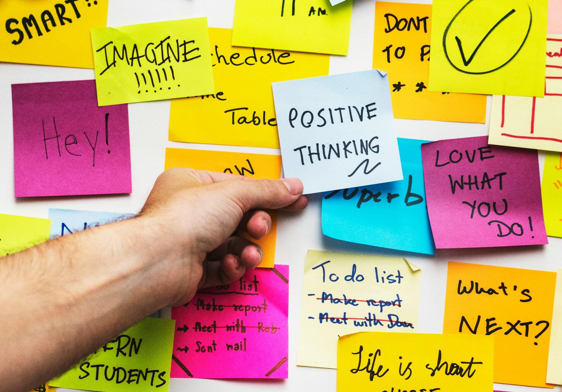 Someone's hand placing a sticky note that says positive thinking.