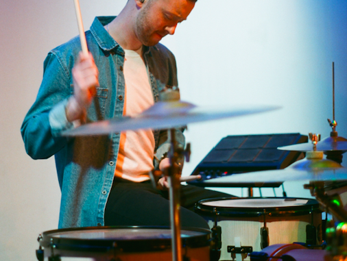 Man standing next to cymbols.