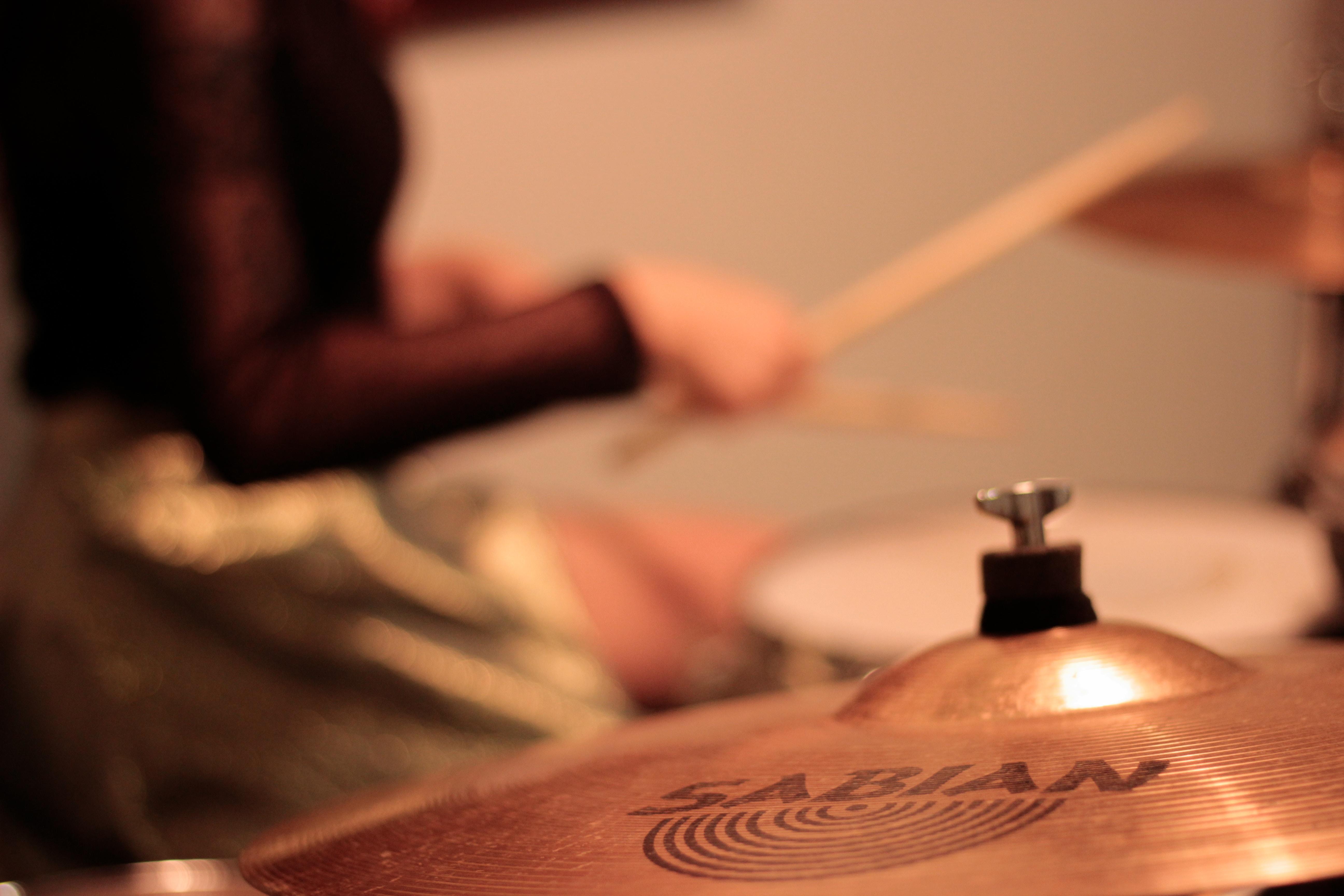 Person sitting next to cymbals holding drumsticks.
