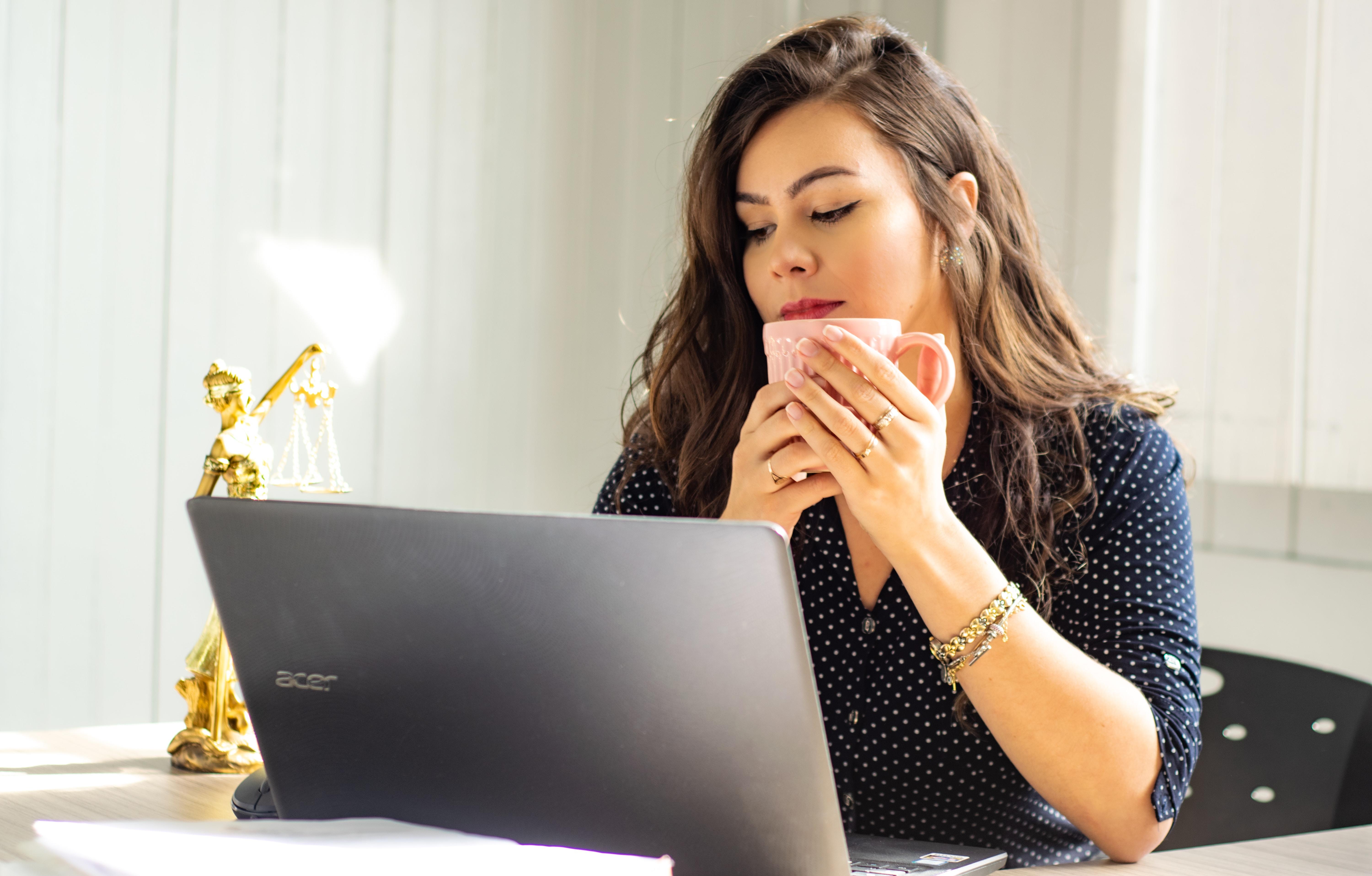 Woman holding a mug staring at a computer screen.