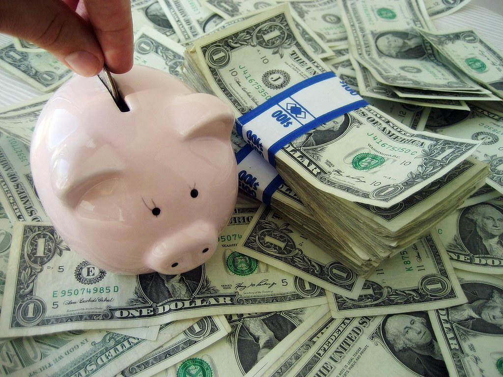 someone putting in money into a piggy bank surrounded by dollars