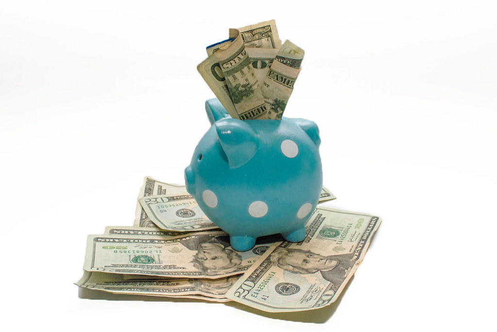 US dollars being crammed into a small piggy bank