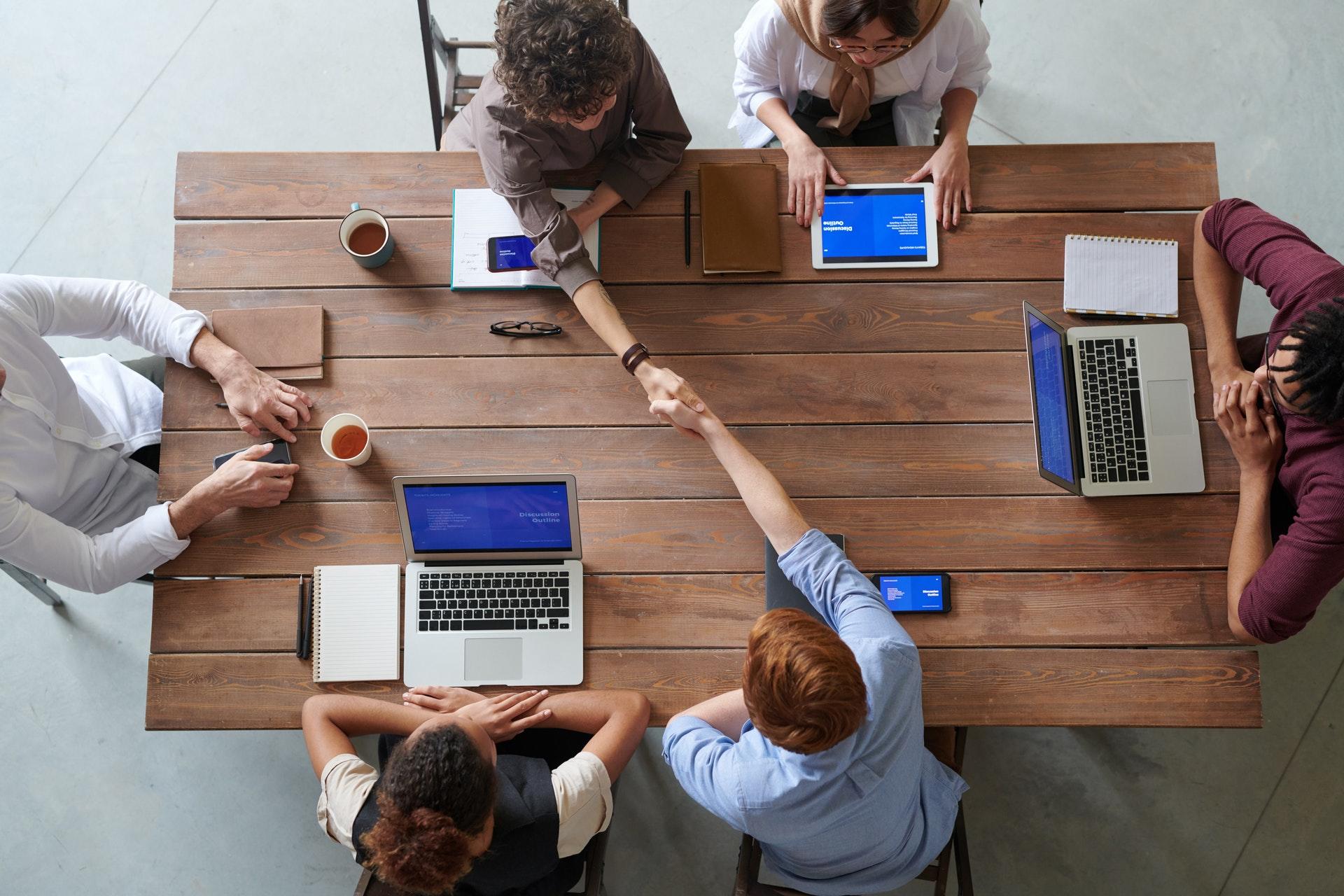 Top down view of several people at a table with laptops.