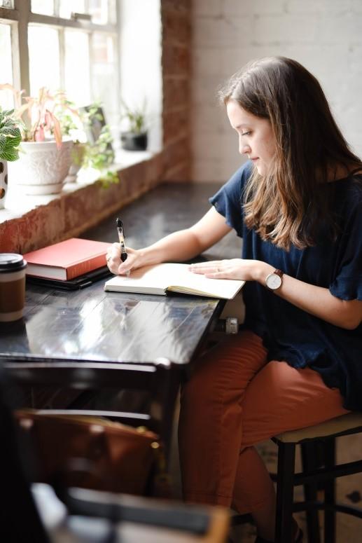 A girl writing notes while studying beside a window