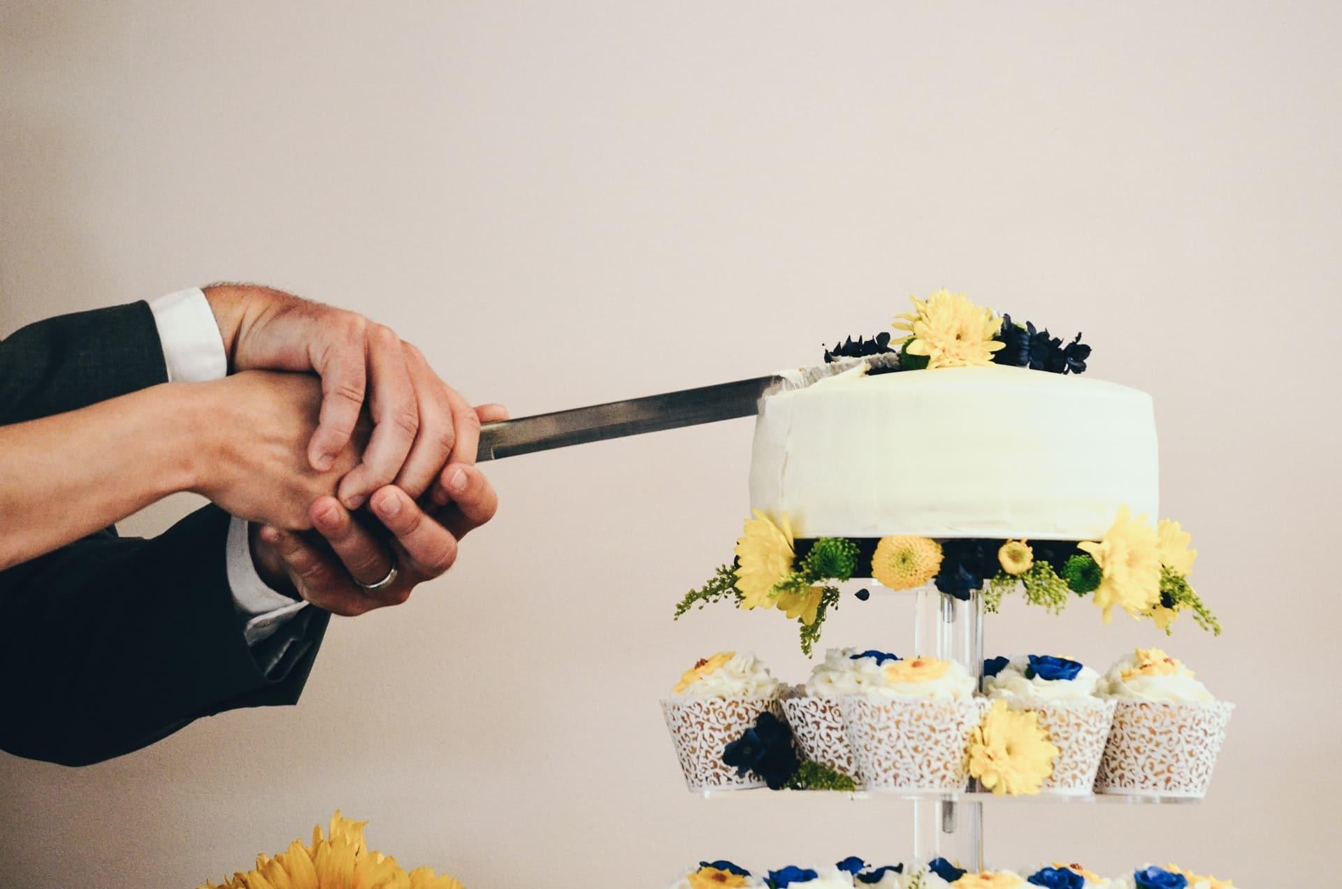 Bride and groom's hands holding a knife to cut a layered wedding cake.