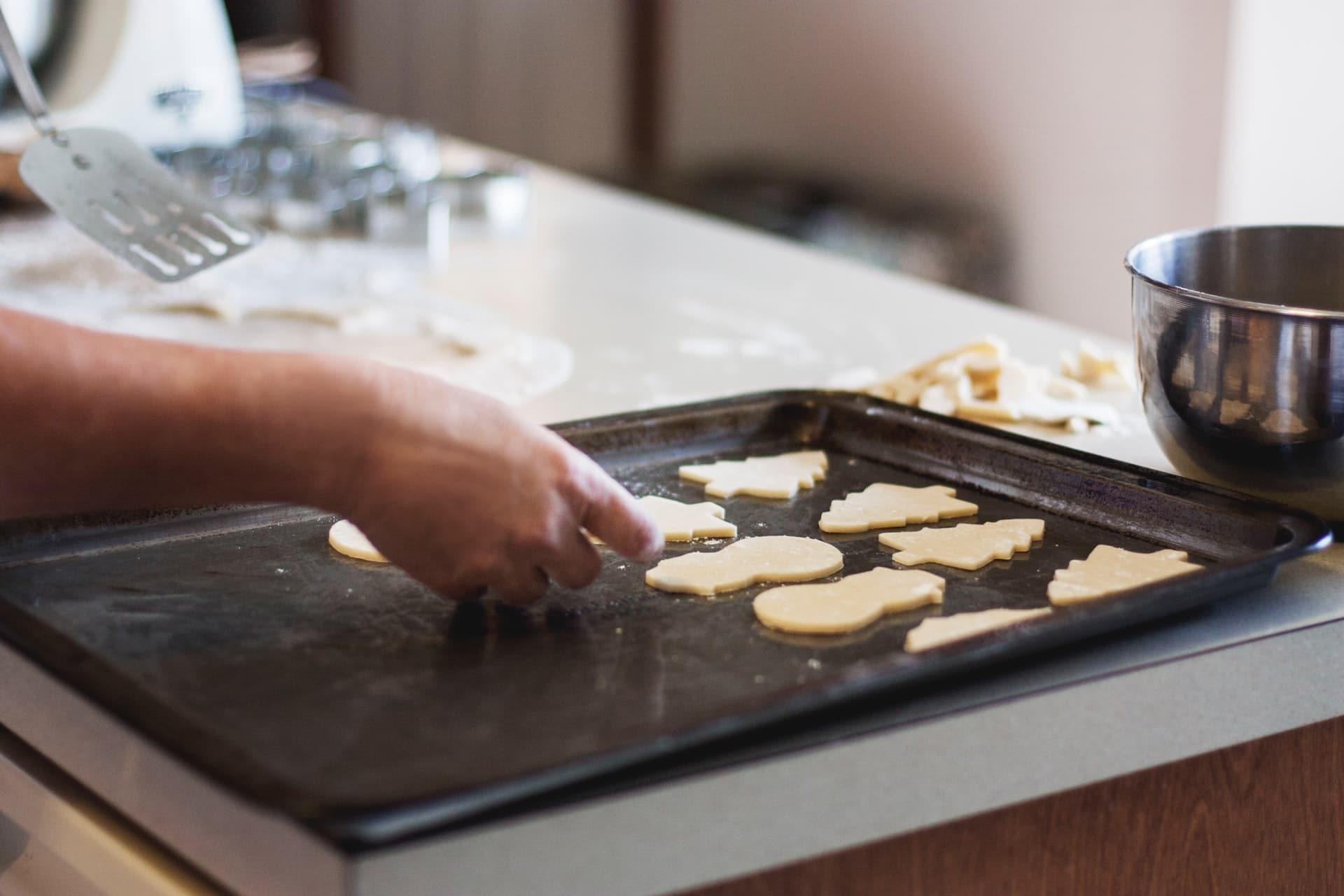 Person's hand putting down cookie shapes on a baking sheet.