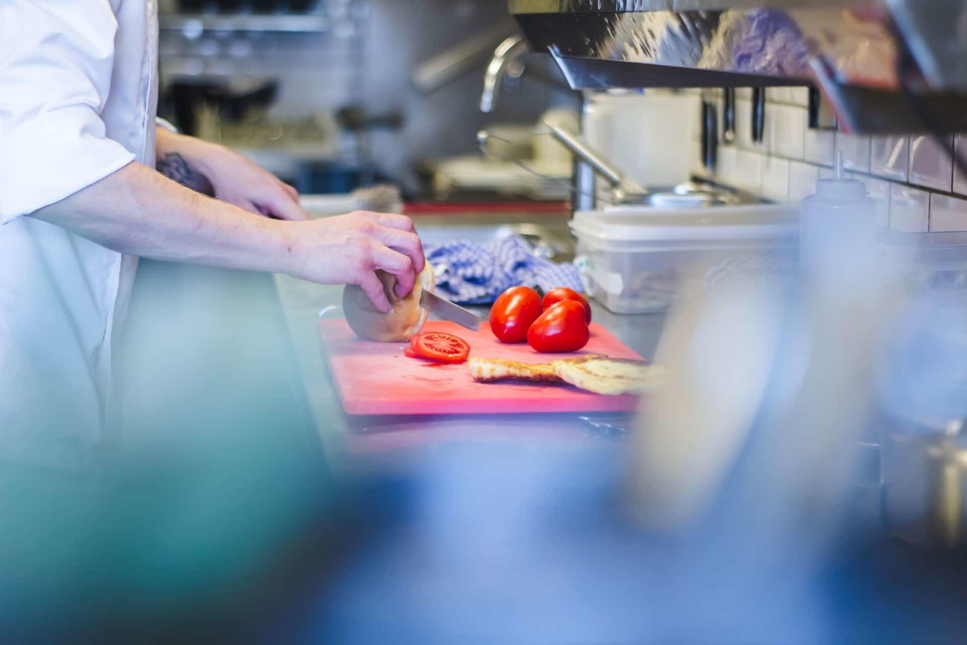 Chef's hands cutting tomatoes in the kitchen.