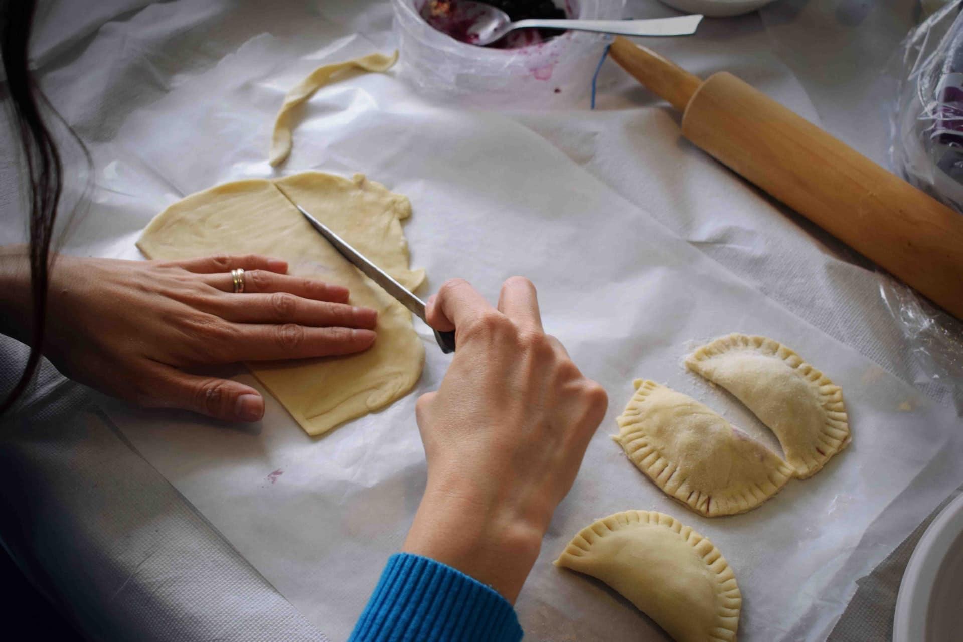 Person's hands cutting dough to make empanadas.