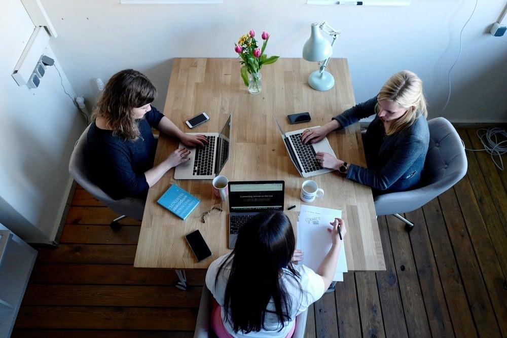 An aerial image of three women sitting in front of laptops.