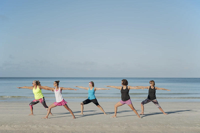 five students perform a yoga pose on the beach. 