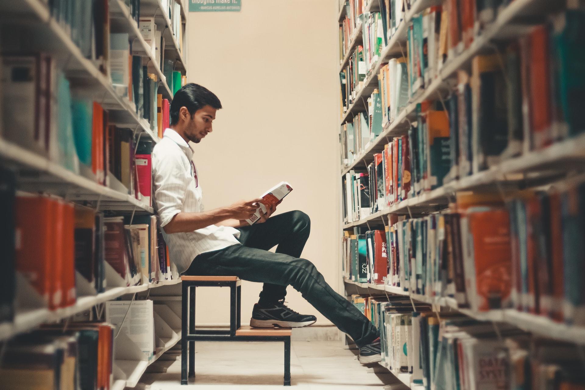 boy sitting on stool in between library shelves