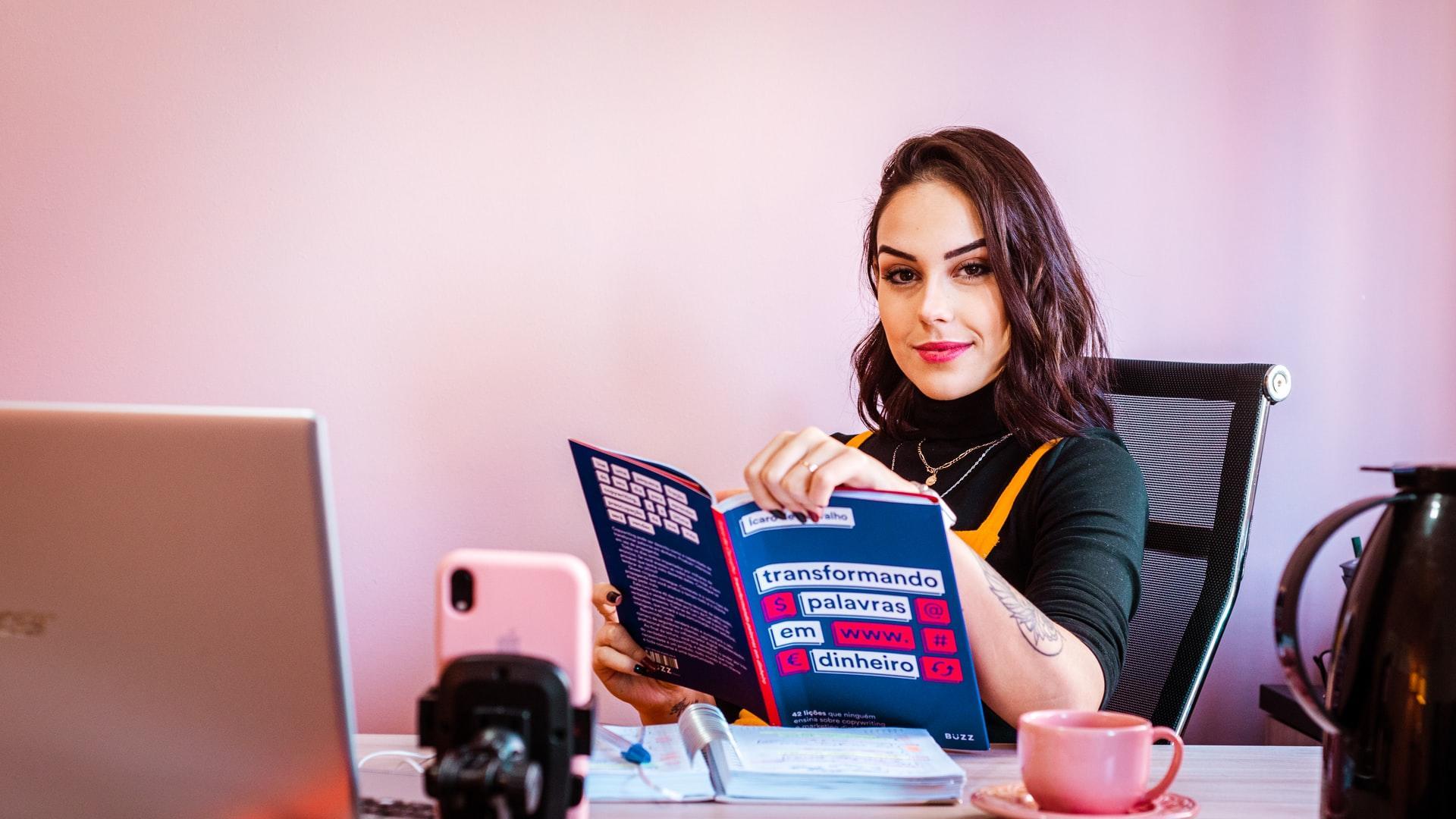 girl sitting at desk reading an open book next to a laptop