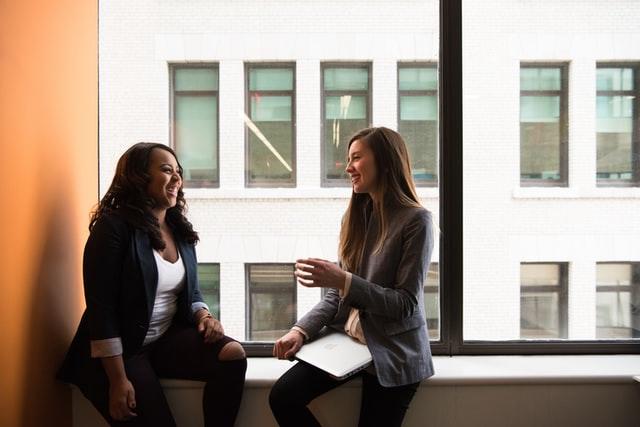 two girls sitting on a window ledge chatting and smiling