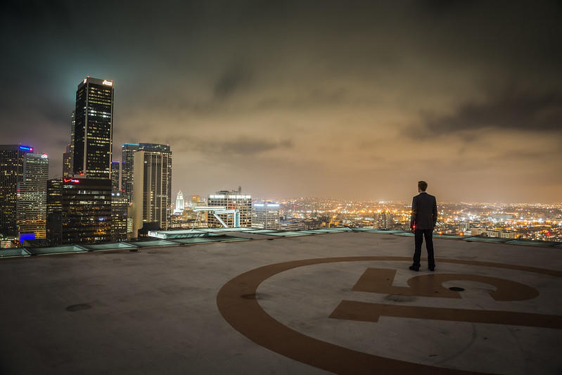 A gentleman stands on a helipad beside the cities skyscrapers.