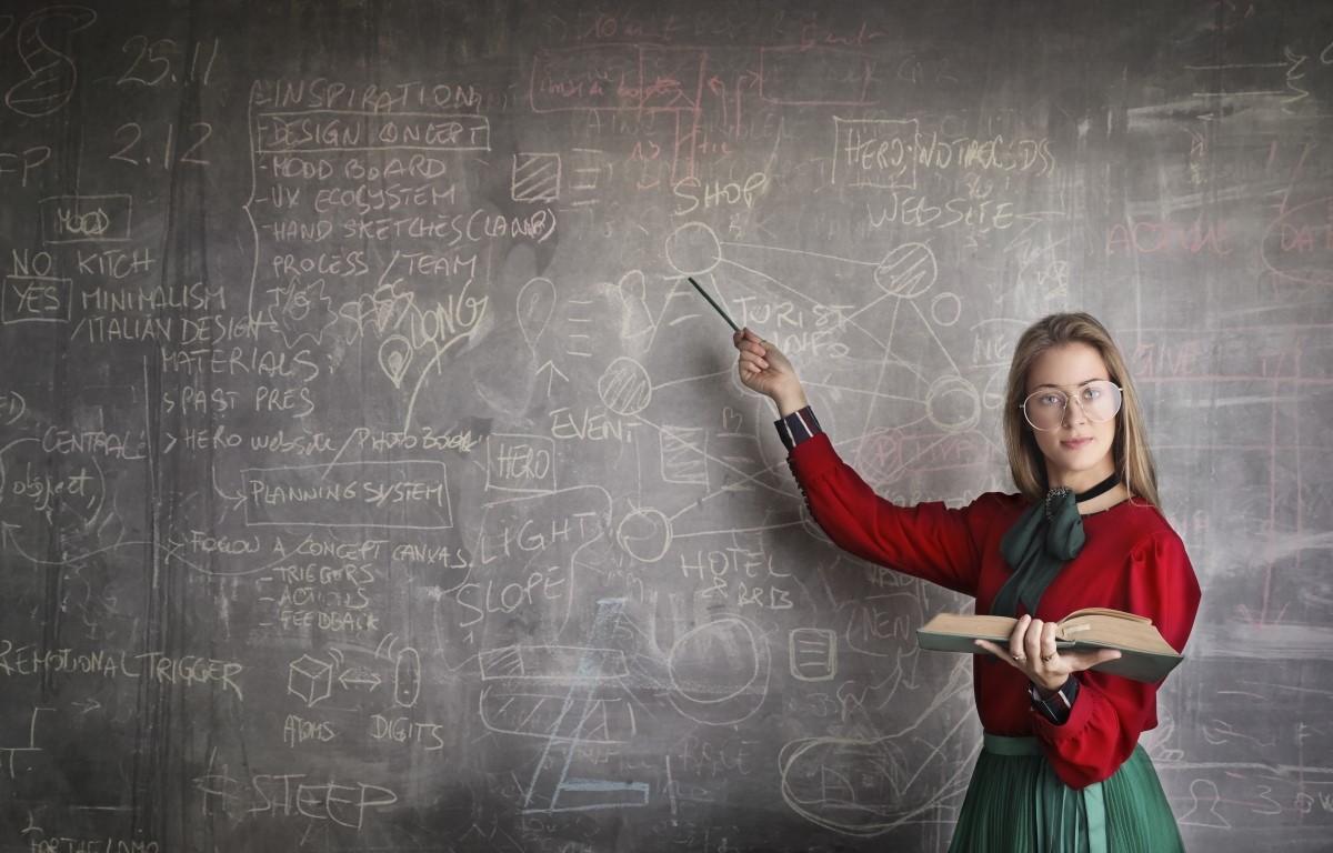 Female Tutor with book pointing at blackboard