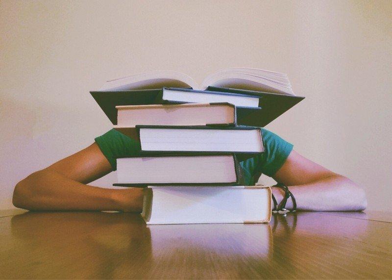 A student sits behind a pile of books.