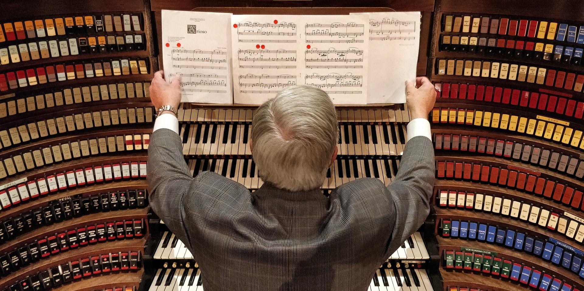 old man looking at music sheets over keyboards
