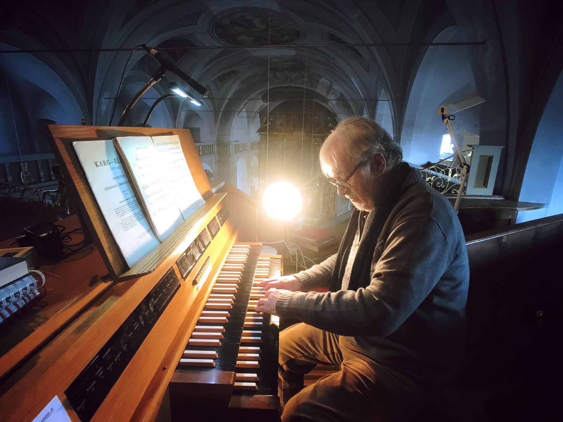 old man playing piano in a dark space 