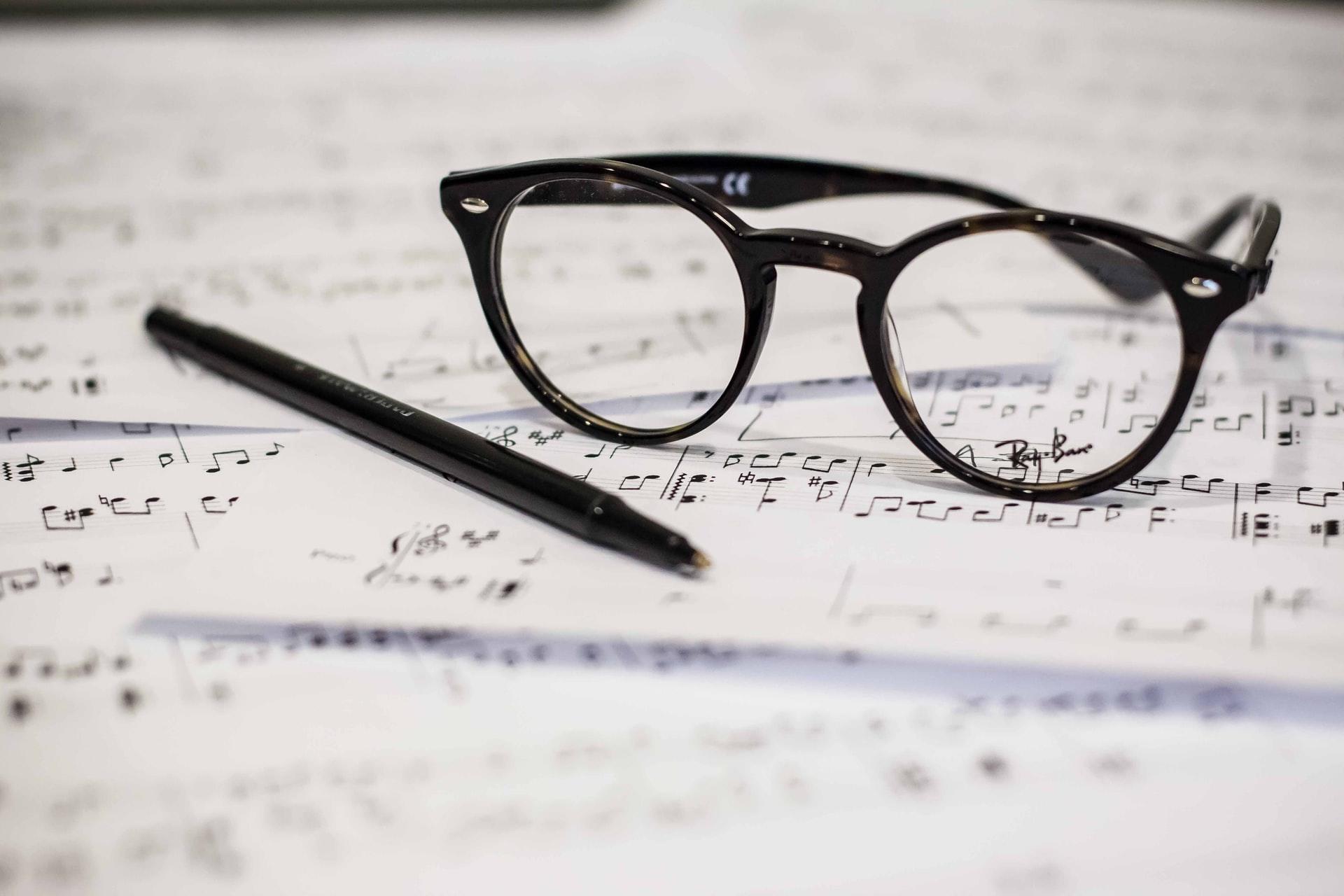 glasses and a black pen on top of music sheets
