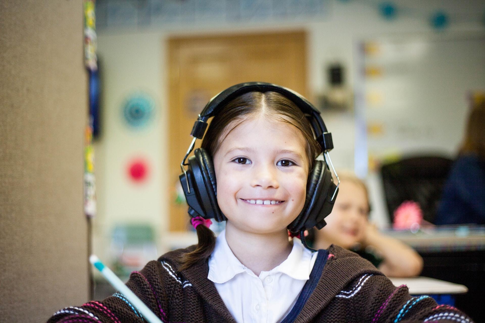 A young girl wearing big headphones, sitting down and smiling