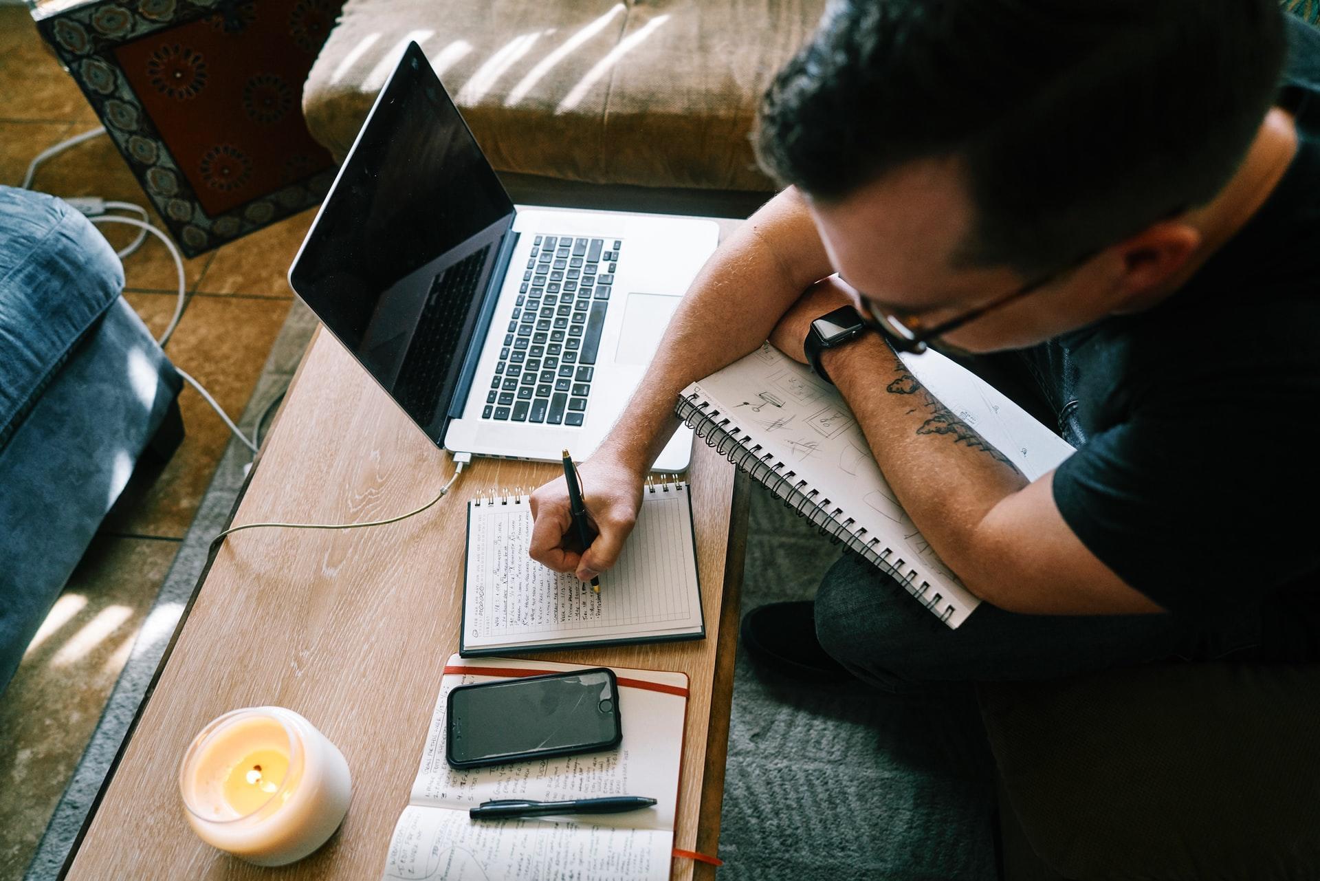 a man sitting next to a laptop writing words in a book
