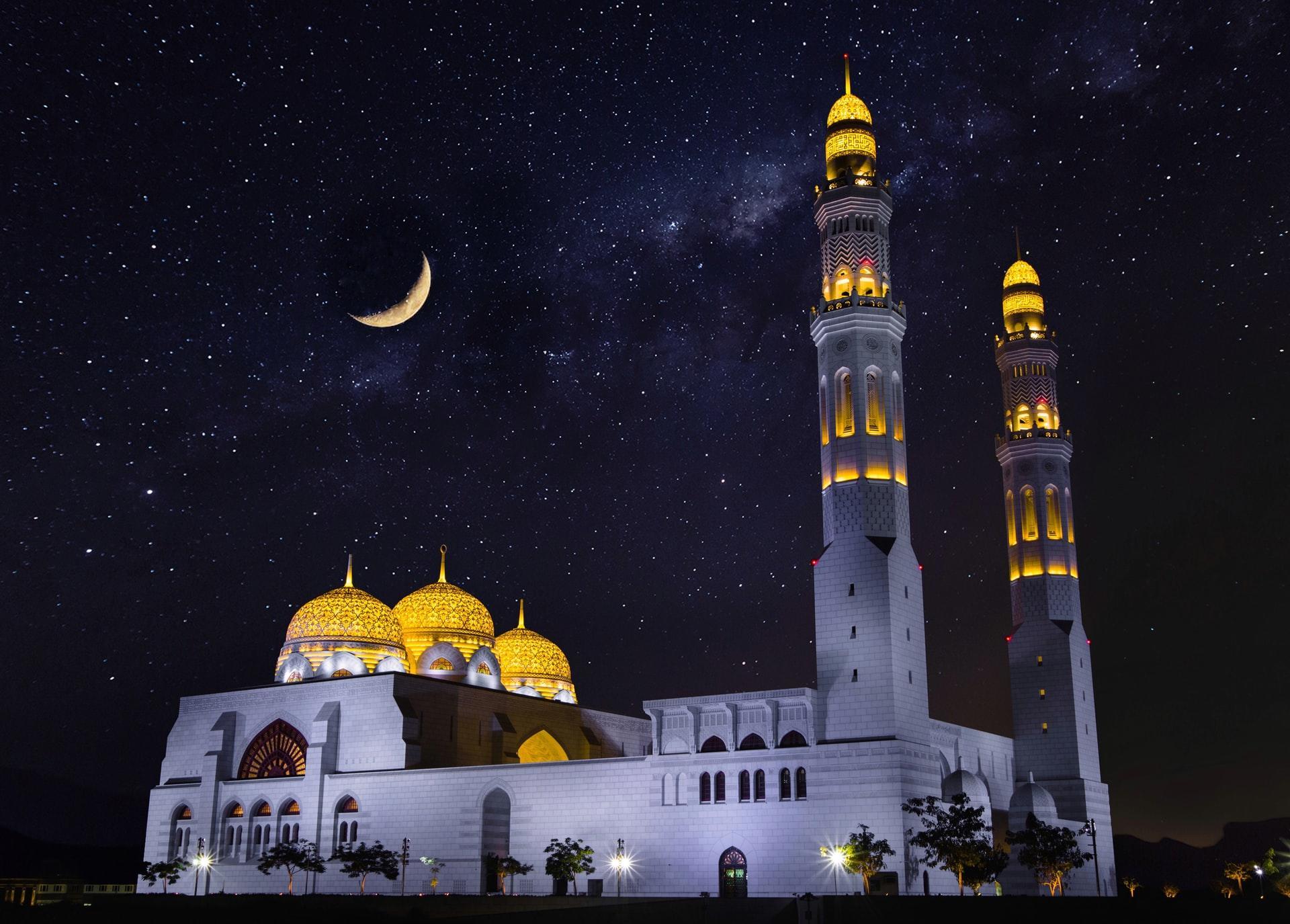 Photograph of large mosque painted white on the outside underneath the night sky